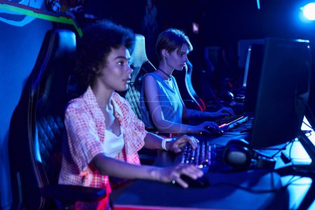 Foto de Centrarse en los juegos de mujeres afroamericanas jóvenes intensamente en una sala de luz azul, concepto de ciberdeporte - Imagen libre de derechos