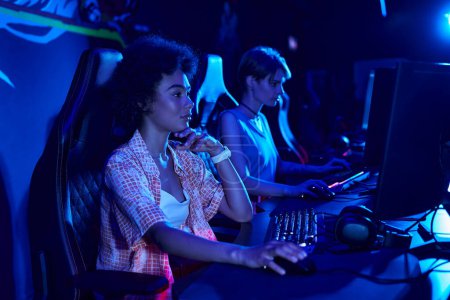 focus on serious african american woman gaming intensely in a blue-lit room, cybersport concept