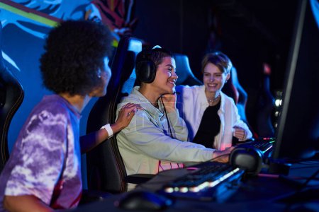 Téléchargez les photos : Heureux femmes interracial zoomers engagés dans des jeux cybersport, en utilisant des ordinateurs et des écouteurs - en image libre de droit