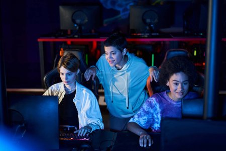 Verschiedene Frauen treiben Cybersport, benutzen Computer und lächeln in einem Raum mit blauem Licht