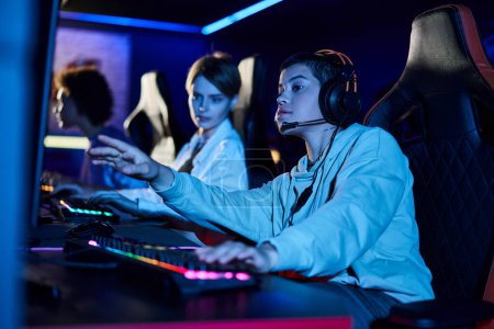 Fokus auf fokussierte Frau mit kurzen Haaren, die in der Nähe von Spielerfrauen auf den Computermonitor blickt