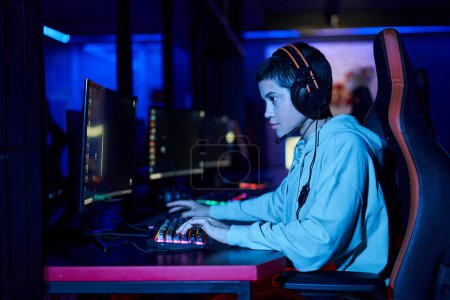 Téléchargez les photos : Se concentrer sur la jeune femme concentrée jouant au jeu dans une pièce éclairée en bleu, cybersport joueuse - en image libre de droit
