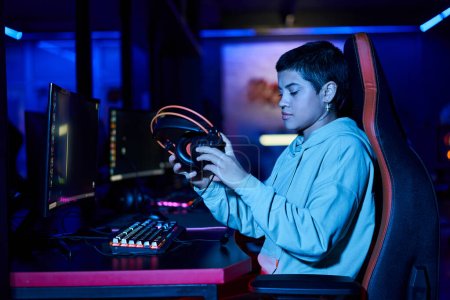 junge Frau setzt Kopfhörer auf den Tisch nach einem Spiel in einem blau beleuchteten Raum, Cybersport