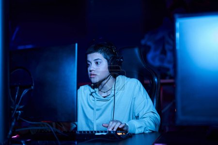 focused young player looking at computer monitor while playing game in a blue lit room, cybersport