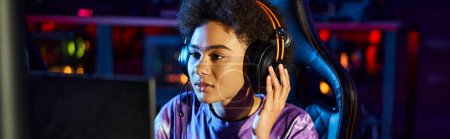 african american gamer in headphones looking at monitor playing computer game, cybersport banner