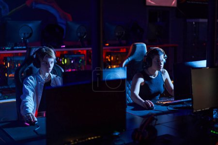 fokussierte Spieler mit Kopfhörern, die auf Monitore schauen, während sie Multiplayer-Computerspiel spielen, Cybersport