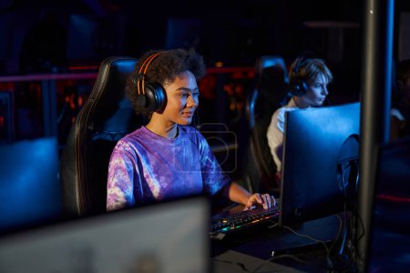 diverse female gamers in headphones looking at monitors while playing multiplayer computer game