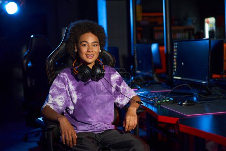 feliz africano americano femenino gamer con auriculares sentado en cómoda silla de juego, cybersport