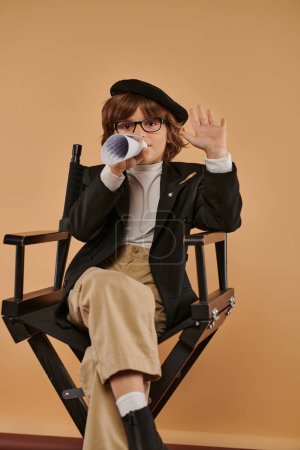 elegante chico en boina se sienta en silla de director, hablando en un pedazo de papel laminado y mostrando cinco