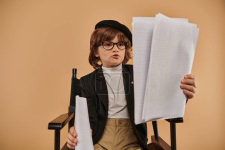busy boy in glasses sits in director chair, looking at papers and absorbed in his reading in studio