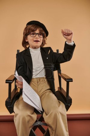 Entschlossener Junge sitzt mit Papieren in der Hand im Regiestuhl, bereit, als Filmemacher die Welt zu erobern