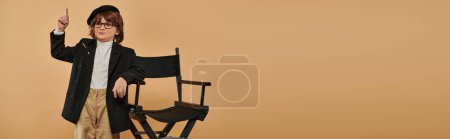 Photo for Boy standing near director chair, with a smile on face showing idea sign,  profession banner - Royalty Free Image