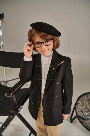 stylischer Junge mit Jacke und Baskenmütze, während er vor grauem Hintergrund lächelt, Kind als Regisseur des Films