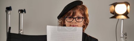 well-dressed kid in glasses and beret reading screenplay, boy as director of filmmaker banner