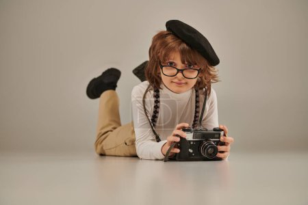 joven fotógrafo en boina y gafas tomando fotos en cámara y tumbado en el suelo, chico creativo