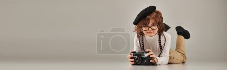 Junge Fotograf mit Baskenmütze und Brille, fotografierend auf dem Boden liegend, Banner