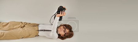 niño feliz captura un momento mientras está acostado en el suelo, niño en boina y gafas con cámara retro, pancarta