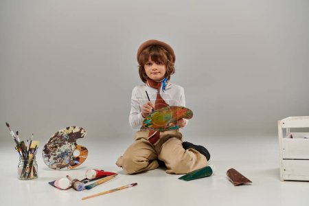Téléchargez les photos : Jeune artiste entouré de couleurs vives et des outils pour la peinture, garçon la création d'un chef-d'œuvre - en image libre de droit