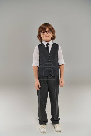 futuro hombre de negocios, niño feliz en traje formal elegante y gafas de pie sobre fondo gris