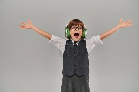 Photo for Joyous boy smiling as raising his arms in triumph while listening to music through his headphones - Royalty Free Image