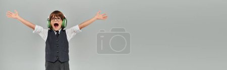 Photo for Joyous boy smiling as raising his arms in triumph while listening to music in headphones, banner - Royalty Free Image