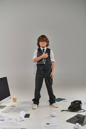 A young professional surrounded by technology and office supplies, holding notebooks on grey