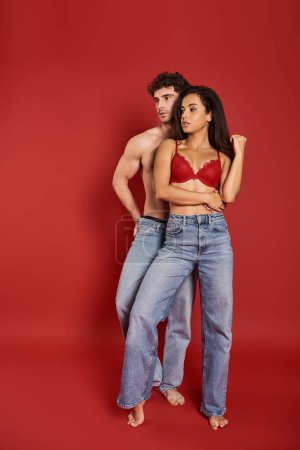 Photo for Handsome shirtless man in jeans posing with beautiful woman in sexy lingerie on red background - Royalty Free Image