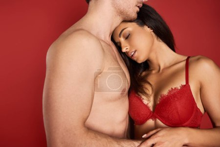 Photo for Beautiful young woman in sexy lace lingerie embracing her muscular boyfriend on red background - Royalty Free Image