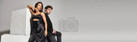 attractive young couple in elegant evening wear posing together near cubes on grey backdrop, banner