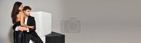 Photo for Handsome man in formal wear embracing beautiful young woman in black dress on grey backdrop, banner - Royalty Free Image