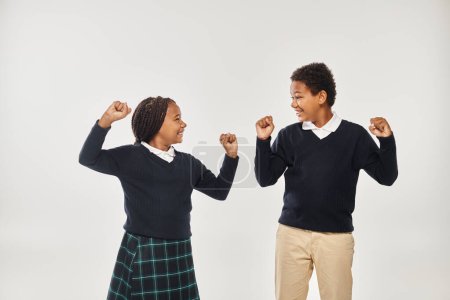 excited african american schoolkids in uniform rejoicing while standing on grey background
