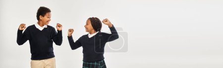 excited african american schoolkids in uniform rejoicing while standing on grey background, banner
