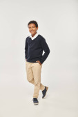 happy african american schoolboy in neat uniform standing with hands in pockets on grey backdrop hoodie #692617446