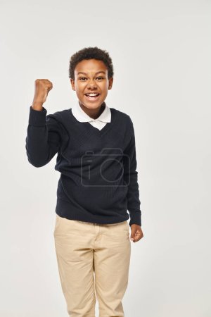 excited african american schoolboy in neat uniform rejoicing while standing on grey backdrop puzzle 692617454