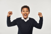 excited african american schoolboy in uniform rejoicing while looking at camera on grey backdrop t-shirt #692617474