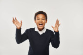 excited african american boy in school uniform rejoicing while looking at camera on grey backdrop tote bag #692617514