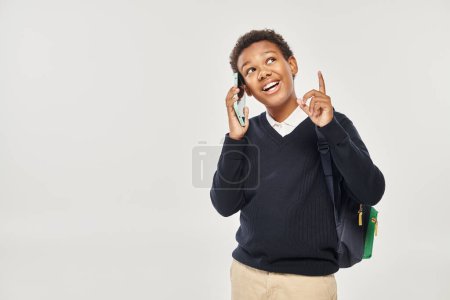 Photo for Happy african american schoolboy in uniform talking on smartphone and gesturing on grey background - Royalty Free Image