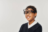 optimistic african american boy in sweater and eyewear holding glasses and looking at camera on grey tote bag #692618798