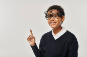 optimistic african american schoolboy in eyewear holding glasses and looking at camera on grey Sweatshirt #692618846