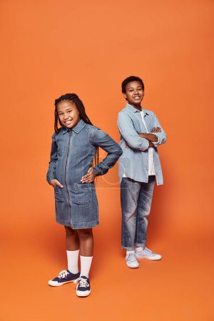 niños afroamericanos felices en traje de mezclilla casual posando juntos sobre fondo naranja