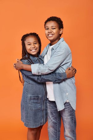 joyeux afro-américain fille et garçon en tenues décontractées étreignant et souriant joyeusement à la caméra