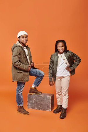 Foto de Alegre preadolescente afroamericano amigos en invierno trajes posando juntos en naranja telón de fondo - Imagen libre de derechos