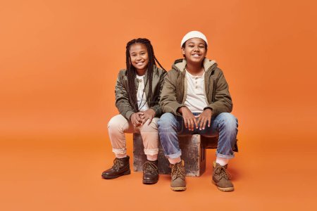 Téléchargez les photos : Gai préadolescent afro-américain garçon et fille assis et souriant heureux à la caméra - en image libre de droit