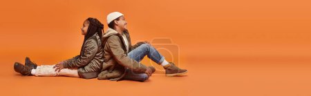 Téléchargez les photos : Préadolescence afro-américaine enfants assis dos à dos sur le sol sur fond orange, bannière - en image libre de droit
