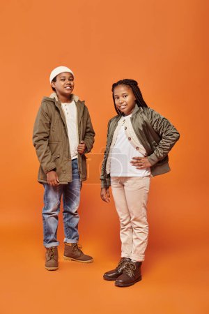 happy preteen african american friends in winter jackets posing together on orange backdrop
