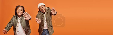 Foto de Niños afroamericanos alegres en trajes calientes posando en movimiento y sonriendo a la cámara, pancarta - Imagen libre de derechos