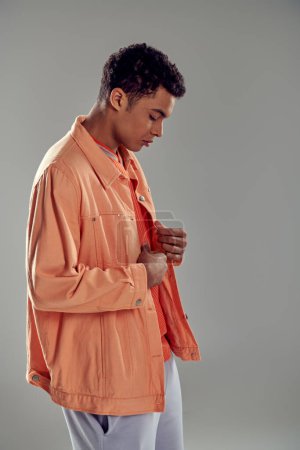 schöner Mann im pfirsichfarbenen Hemd steht vor grauer Wand und zeigt seinen makellosen Sinn für Mode