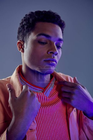 retrato de hombre afroamericano guapo en camisa de melocotón posando sobre fondo gris con luz azul