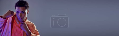 Téléchargez les photos : Bannière de beau mec afro-américain en chemise pêche regardant caméra sur gris avec lumière bleue - en image libre de droit