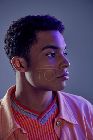 Porträt eines hübschen afrikanisch-amerikanischen Typen im Pfirsichhemd, der mit blauem Licht auf grau blickt